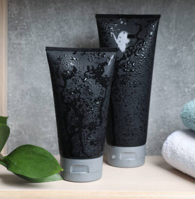 Wet black tubes with men's cosmetic products and towels on wooden shelf